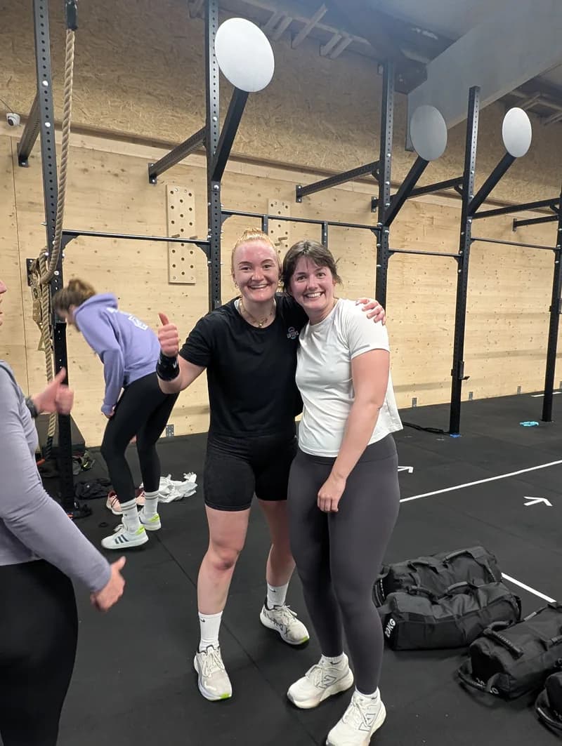 Zwei Teilnehmerinnen stehen nach der HYROX® Race Simulation Arm in Arm in der Box von AMITY Athletics in Dülmen und lachen