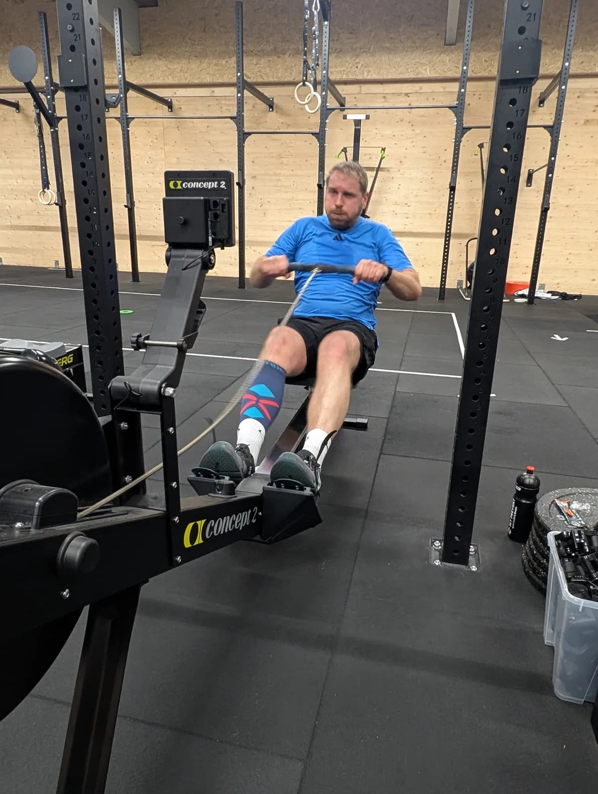 Athlet zieht auf dem Concept2 RowErg, im Hintergrund das Rig mit Ringen — AMITY Athletics in Dülmen