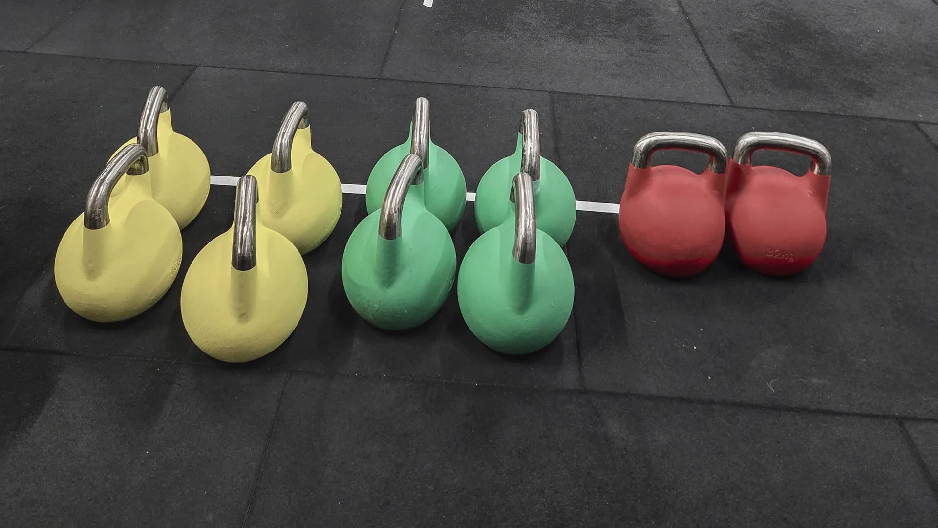Gelbe, grüne und rote Kettlebells in einer Reihe auf dem dunklen Hallenboden von AMITY Athletics in Dülmen