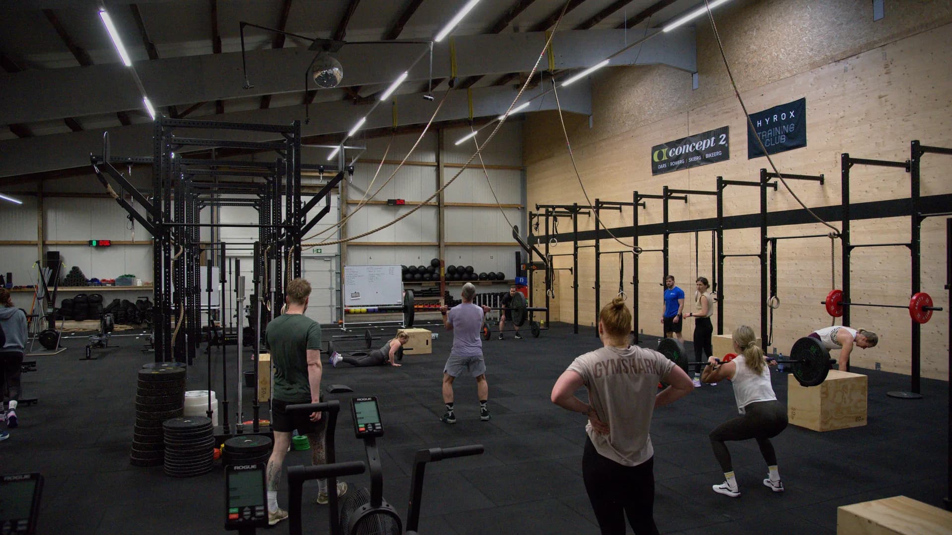 Offene Trainingsfläche von AMITY Athletics in Dülmen während einer Class: Rigs, Concept2® Ergometer, Boxen und die Banner von Concept2® und HYROX® Training Club an der Holzwand